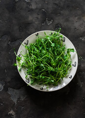 Pea sprouts in a bowl on a dark background, top view