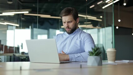 Stressed businessman sits at his desk, stressed, as he reacts to a disappointing outcome on his laptop. Problem failure search information trouble with documents difficulties financial mistake