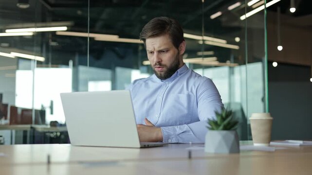 Stressed businessman sits at his desk, stressed, as he reacts to a disappointing outcome on his laptop. Problem failure search information trouble with documents difficulties financial mistake