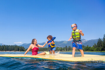 Family and kids playing together on a floating water pad or foam floating mat at a beautiful scenic mountain lake during the summer © Brocreative