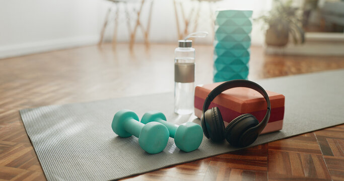 Headphones, mat and dumbbells with water bottle of fitness equipment or interior on floor at home. Empty room or space with headset, weights or liquid for health, wellness or tools for exercise