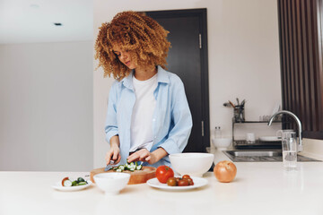Woman preparing healthy meal in modern kitchen with curly hair, cutting vegetables on wooden board