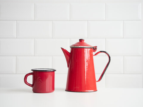 old fashion red enameled steel coffee pot and mug on table with white tile backgrounds and copy space. Concept of kitchen utensils and coffee