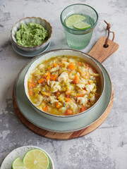savory vegetable and pasta soup dish called minestrone, typical Italian cuisine. Served at the table with green pesto sauce, glass of water and lime slices.