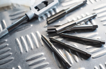 Tapped Hole or Threaded Hole tools on Diamond metal plate ,screw hand tap cutting tool. tap and drill bit making hole.selective focus