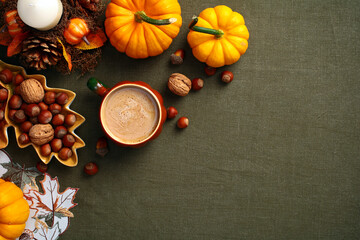 Flatlay composition with pumpkins, coffee cup, nuts, acorns, candle on green textile desk table. Hygge style, cozy autumn holiday concept. Flat lay, top view, overhead.