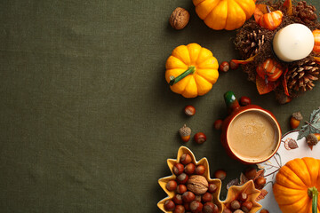 Autumn desk top view. Flat lay composition with pumpkins, coffee cup, maple leaf shaped plate with nuts, candle on green table cloth.