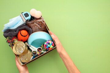Donation box with pet supplies and food in female hand over green background. Pet care, charity,...