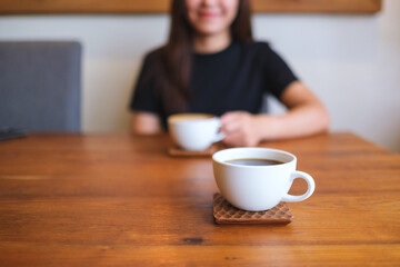 Closeup image of a young woman holding and drinking coffee with friend