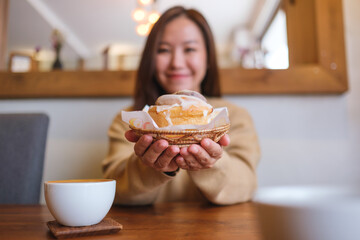 Blurred  image of a young woman holding and serving a piece of cinnamon roll with coffee cup on the table