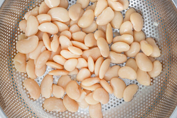 Straining butter beans in a metal colander strainer. Vegan healthy diet food ingredients.