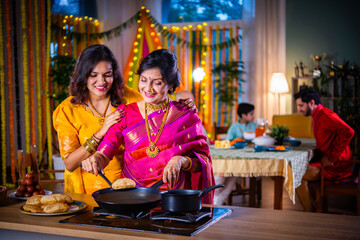 Indian old woman and young daughter in traditional cloths cooking food for Diwali festival at home