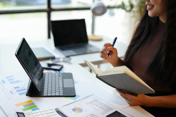Young woman working on laptop in office Asian businesswoman sitting and taking notes in a notebook Thinking of ideas at your desk Beautiful independent woman working online with paperwork.