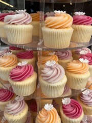 Stand with colorful cupcakes, orange. and pink cupcakes with cream topping and a white flower