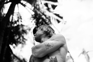 Tattooed man with a naked torso against the backdrop of palm.