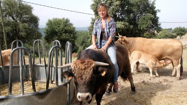 A woman confidently rides a large bull in a beautiful countryside, showcasing her adventurous spirit and bond with animals.