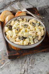 Salad with chicken, prunes, boiled eggs and fresh cucumber dressed with mayonnaise close-up in a bowl on a wooden board. Vertical