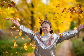 cheerful girl in autumn park throwing yellow leaves in the air