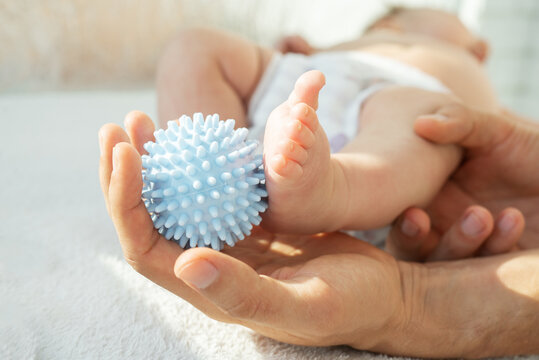 Dad making massage baby legs with a massage ball. Sensory, tactile development, activity muscles. Concept of taking care baby, fine motor skills. close up.