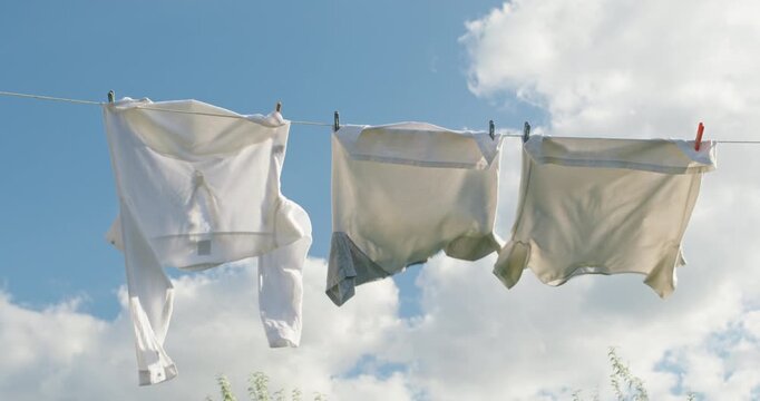 Three white shirts sway on a clothesline under a clear sky with soft clouds.