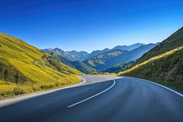 Fototapeta premium A scenic mountain road winding through vibrant green hills under a clear blue sky, perfect for travel and adventure themes.