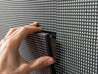Close-up of a man's hand installing a square LED module into its place on the surface of a large...