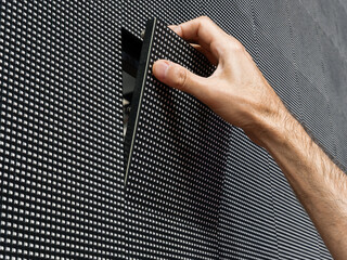 A man's hand removing a square LED module from its place on the surface of a large LED screen for...