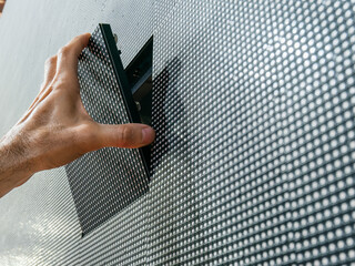 A man's hand installing a square LED module from its place on the surface of a large LED screen after repair and maintenance