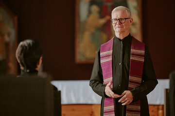 Silver-haired pastor dressed in black robe saying prayer during funeral