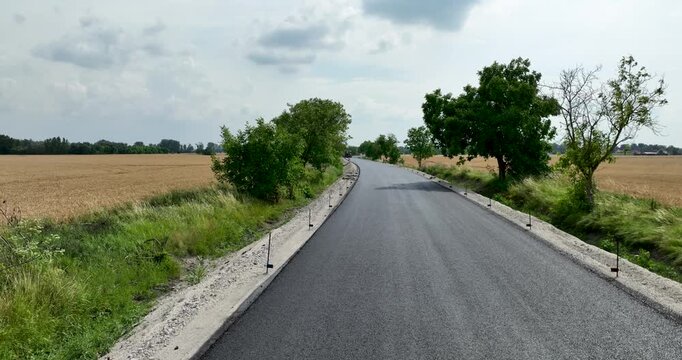 Aerial views of fresh asphalt road construction outside during spring/summer. Flying above agricultural land and newly reconstructed roads