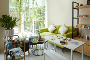 Cozy living room featuring vibrant green sofa, decorative pillows, and modern furniture. Sunlight streaming through large windows, illuminating lush indoor plants and stylish shelving unit
