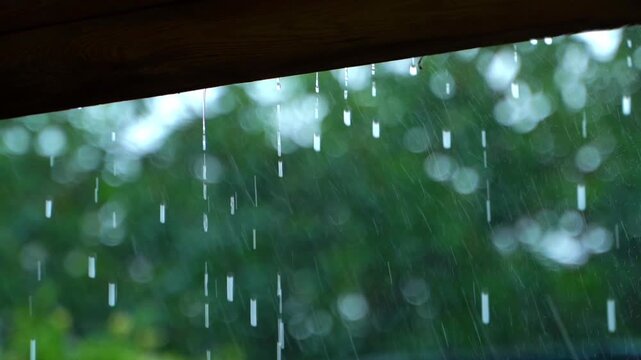 Drops flow from the roof during rain in slow motion, on a blurred background