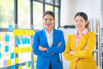 Two Asian businesswomen use laptop and tablet to collaborate in a productive conversation with colleagues while analyzing documents, financial graphs, working in the office.