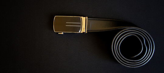 Black leather men's belt with automatic golden buckle lies on a dark background. Photo. Copy space