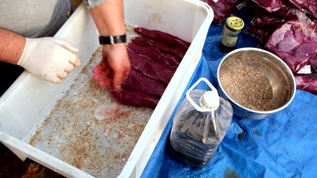 Venison steak pieces stacked together in container for curing to make biltong