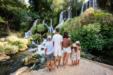 Family enjoying a day by a beautiful Kravice waterfall in a lush green forest, creating lasting...