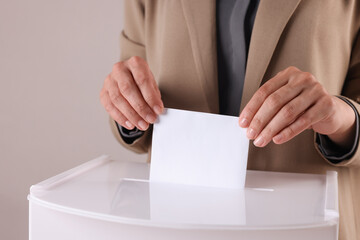 Woman putting her vote into ballot box against grey background, closeup