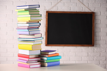 Stacks of many colorful books on white wooden table in classroom. Space for text