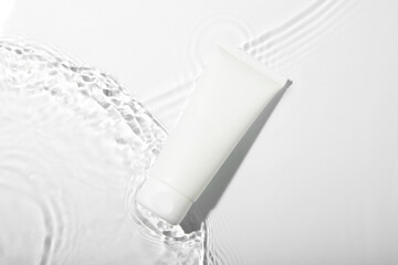 Cosmetic product. Tube with cream in water on light background, top view