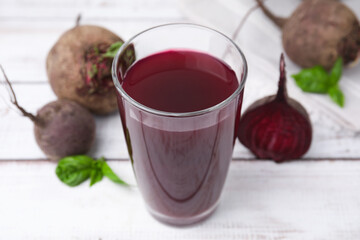 Fresh beet juice in glass and ripe vegetables on light wooden table, closeup