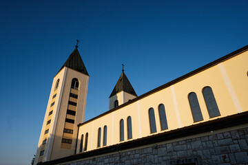 Beautiful Saint James church architecture with two steeples and a clear blue sky in the background, highlighting a serene and religious atmosphere in a tranquil setting in Medjugorje.