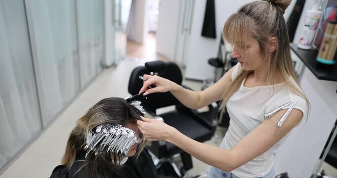 Hairdresser applies bleach powder to woman hair and wraps it in foil