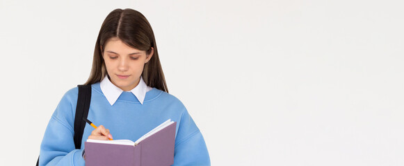 Happy teen student girl wear blue sweatshirt and backpack hold book write down lesson in exercise...