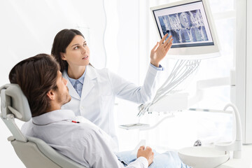 Pretty dentist showing his patient x-ray results, on modern lcd display, free space