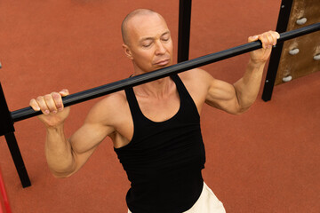 Athlete muscular fitness male pulling up on horizontal bar at street gym. Outdoors. Summer. Workout routine.