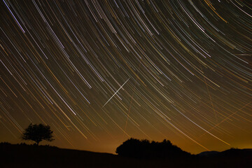 Star trails of a Milky Way with meteor, shooting stars and countryside silhouettes.