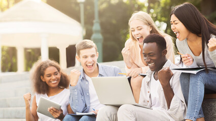 Group of multiracial students celebrating success, checking exam results online, spending time in...