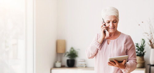 Busy senior woman consulting client on phone and reading contract on digital tablet at home, copy...