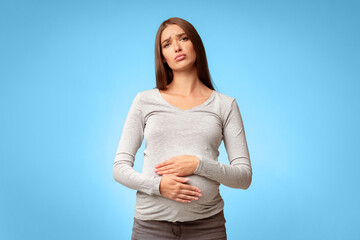 Stomachache During Pregnancy. Unhappy Pregnant Lady Touching Aching Belly Standing Over Gray Studio Background.