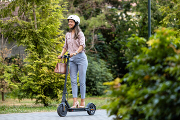 Businesswoman riding electric scooter through the park commuting to work.